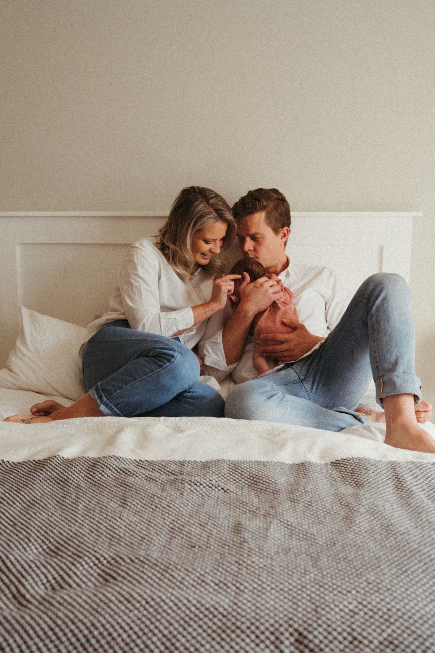 Intimate lifestyle portrait of a couple in white and denim lounging on bed together.