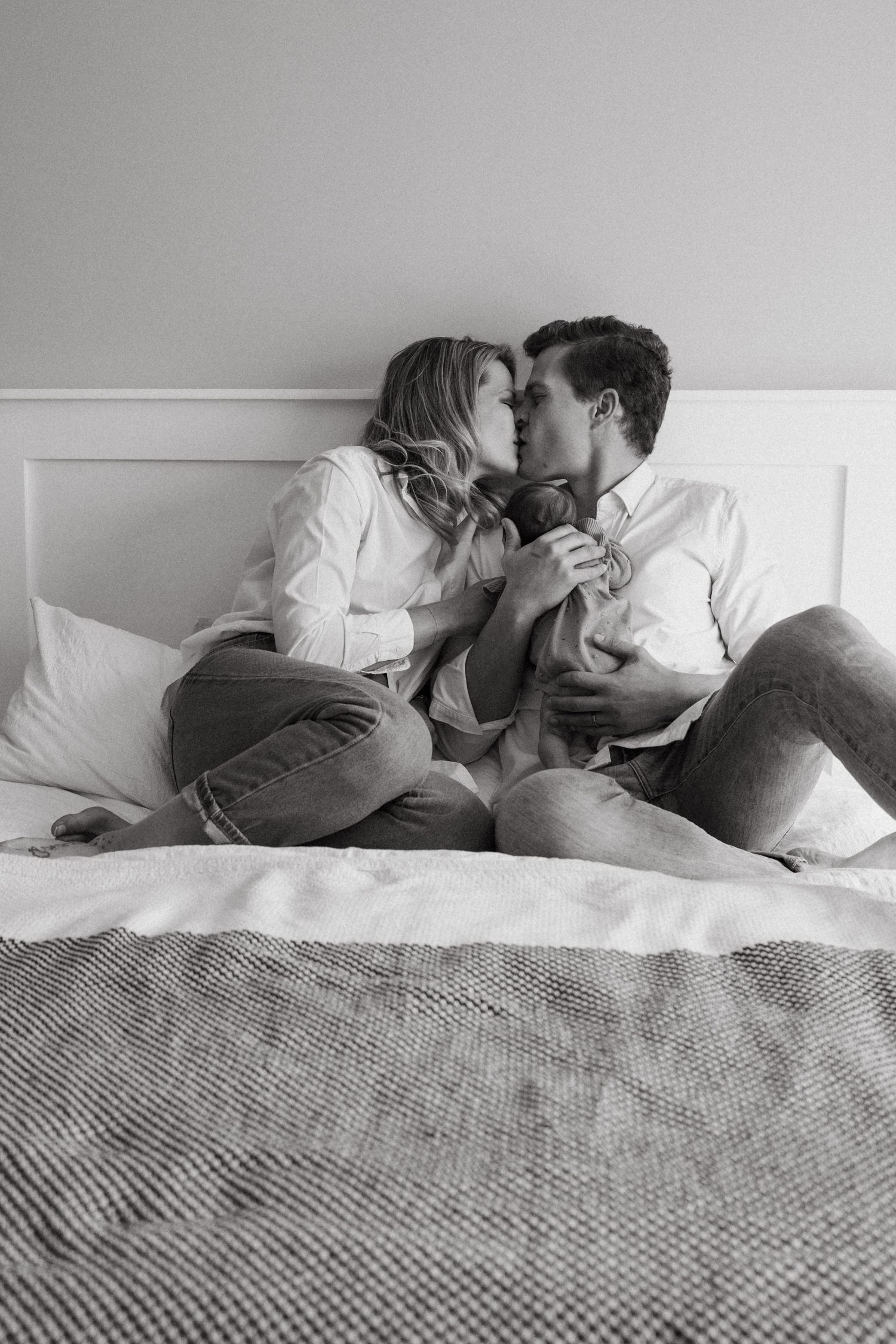 Couple lying together on a textured gray bedspread sharing tender moments.