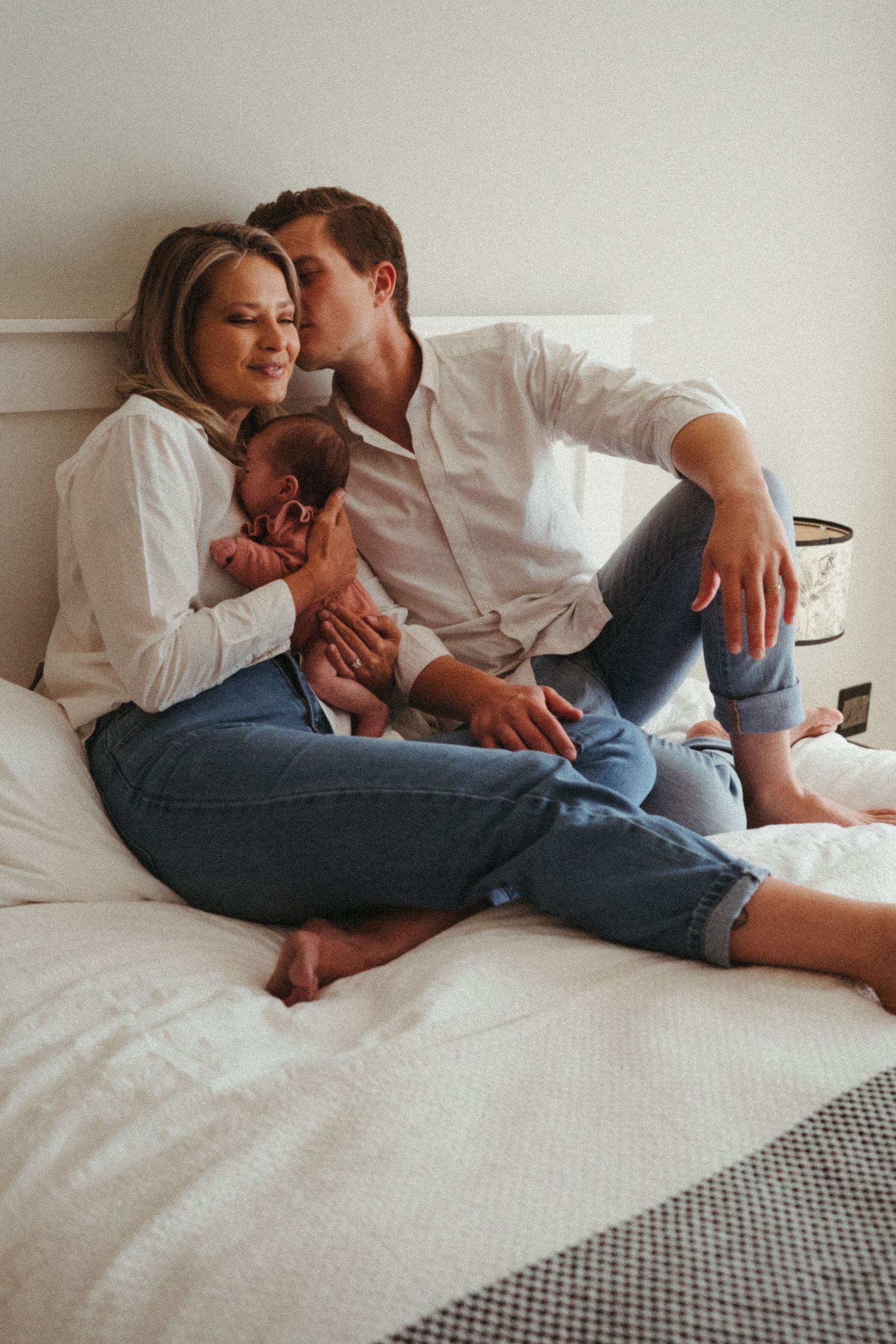 Family portrait showing parents cuddling with their newborn on white bedding.