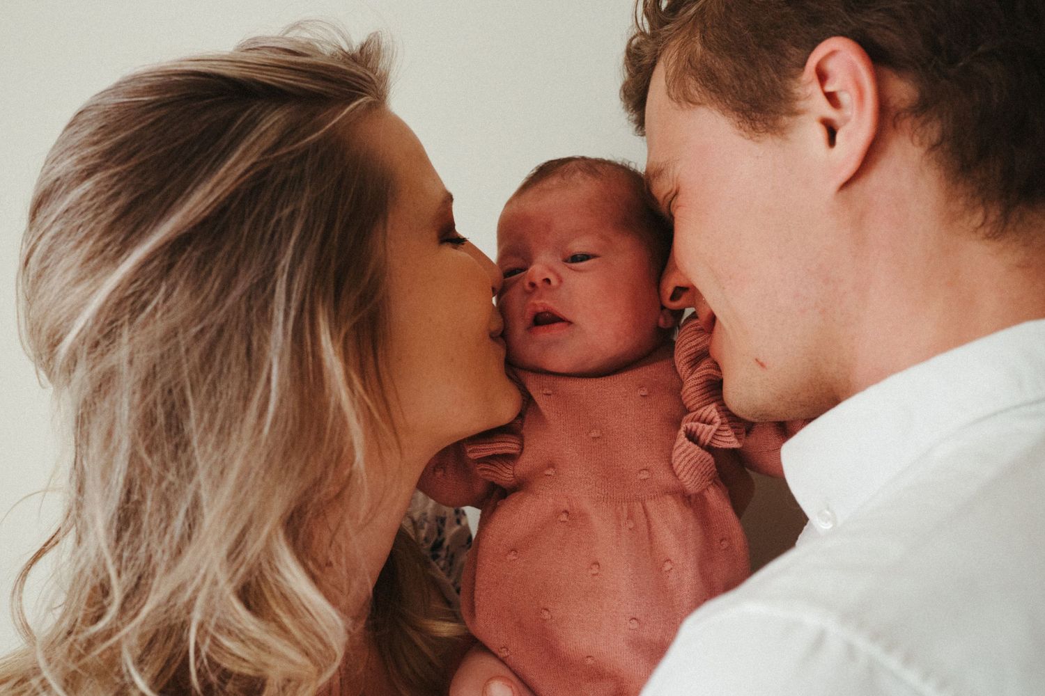 Intimate family moment as parents share loving kisses with their newborn baby.