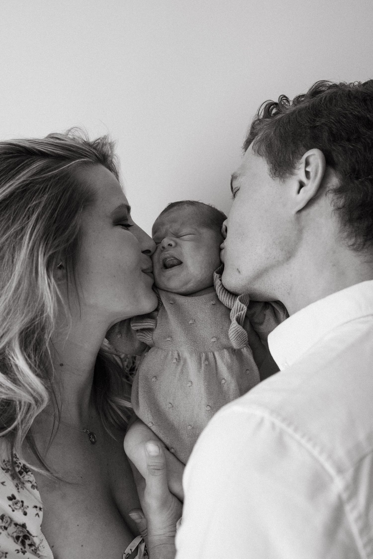 Black and white portrait of parents kissing their newborn baby from both sides.