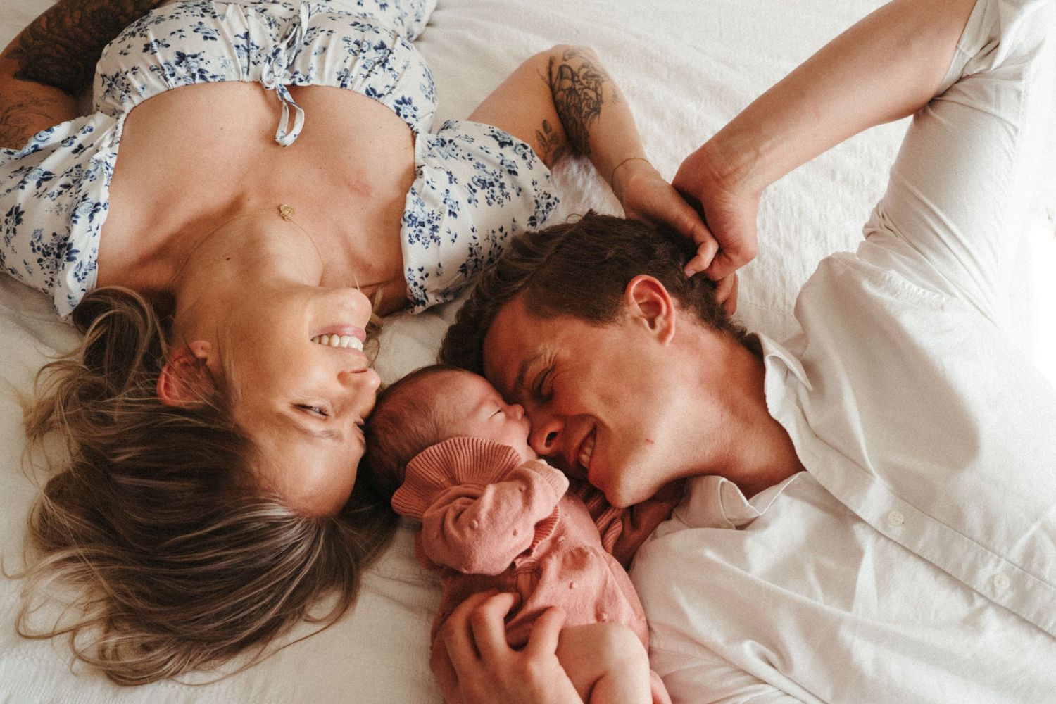 Parents lying on bed with newborn baby between them sharing intimate family moment.