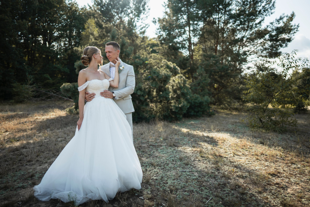Ein Brautpaar in eleganter Hochzeitskleidung posiert in einem malerischen Wald während der goldenen Stunde – romantische Hochzeitsfotografie