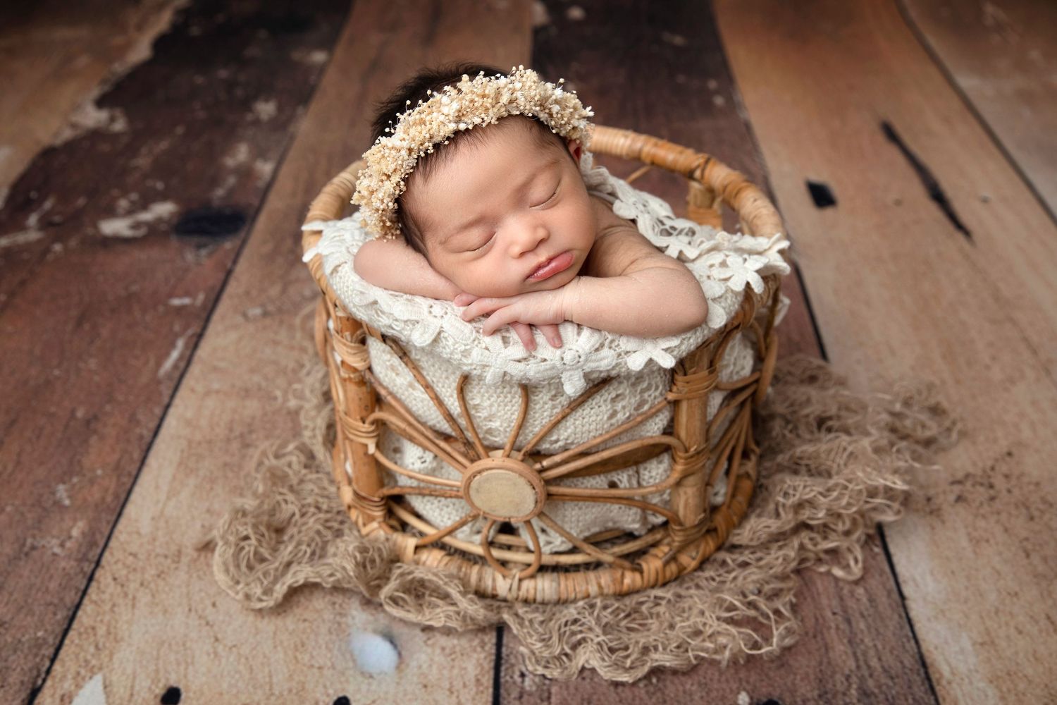 Newborn wrapped in gray knit blanket with lace bonnet on textured fur background.