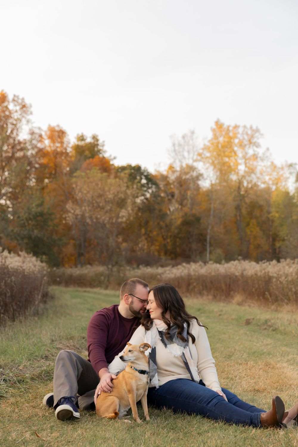 couple sitting on a walking path with autumn leafs behind them at cranberry lake park in Oakland township