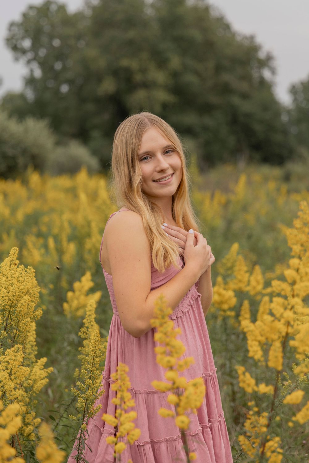 teenage girl wearing a pink dress standing in a field of yellow flowers in september