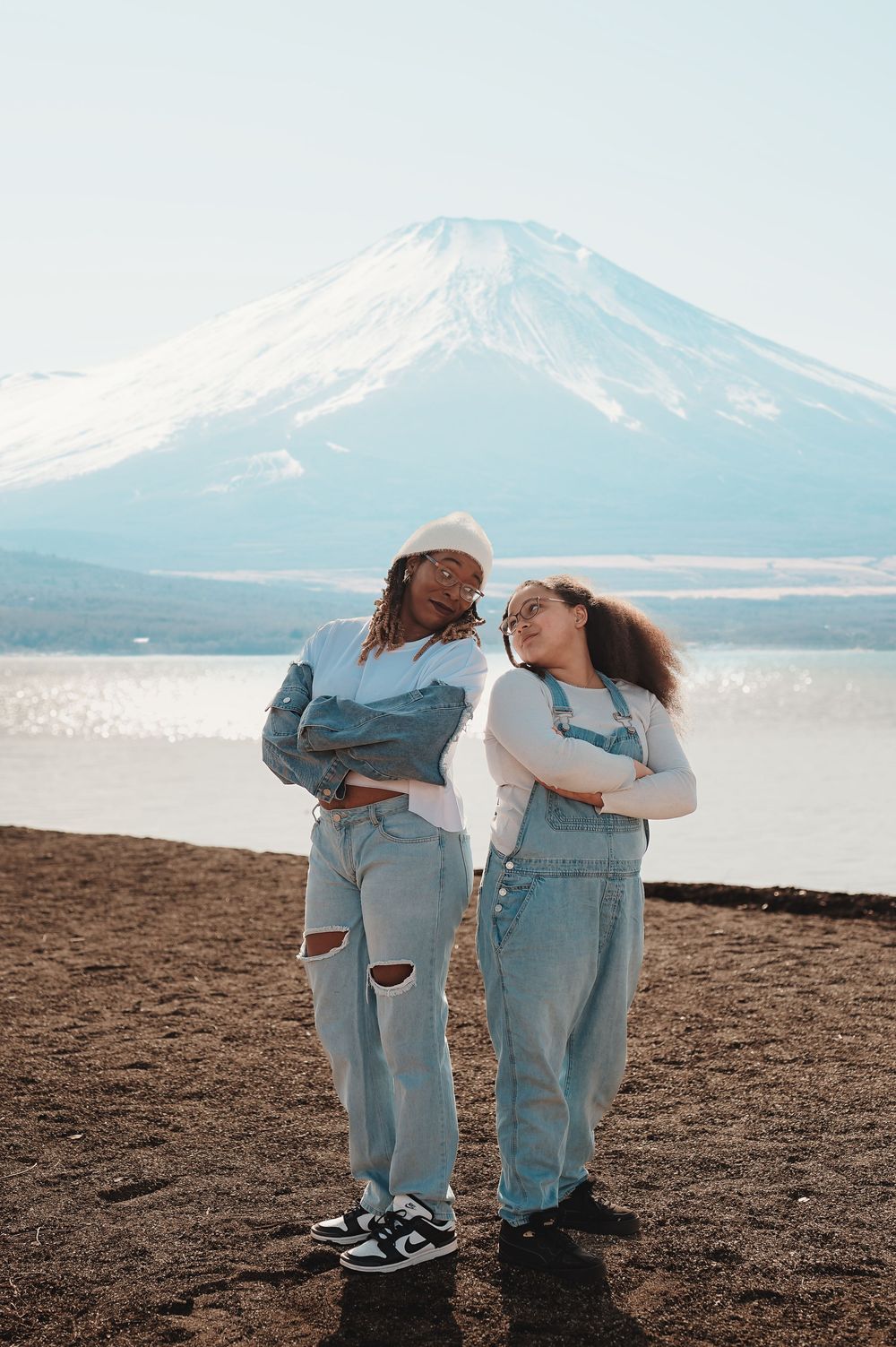 Two people in matching denim outfits stand against a scenic mountain backdrop by a lake.