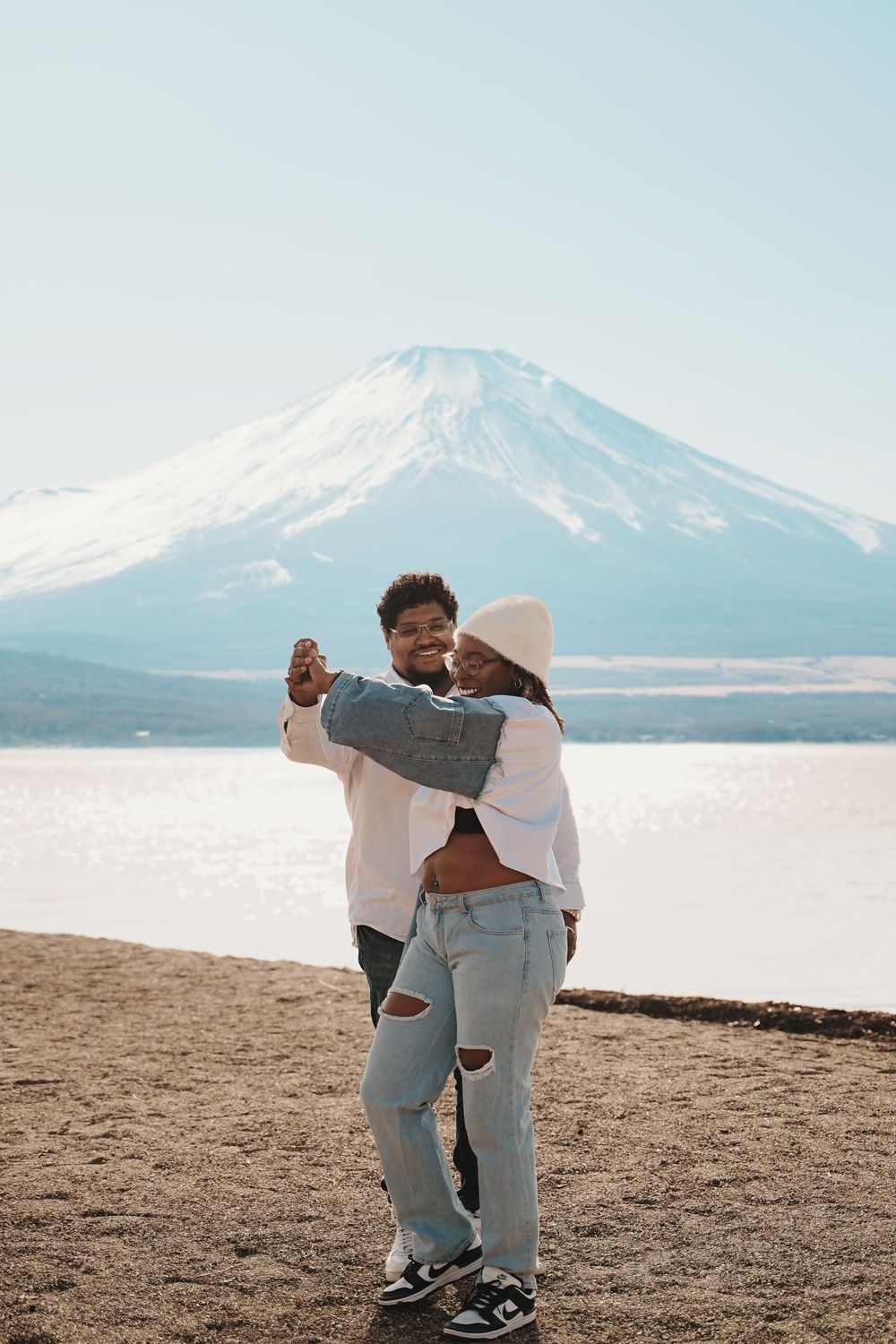 A couple shares an intimate moment on a sandy beach with majestic Mount Fuji rising in the background.