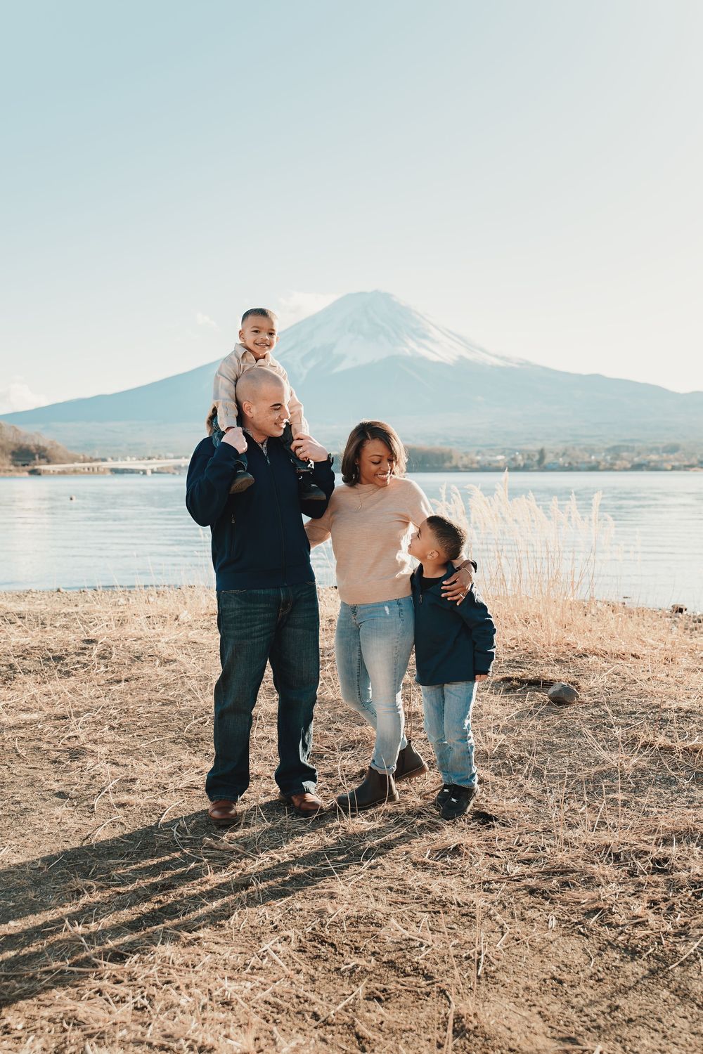 A family stands together on the shore of a lake with Mount Fuji visible in the background in Japan.