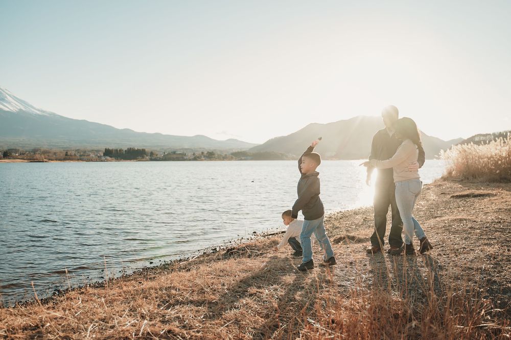 Beautiful sunset scene at a lakeside beach with silhouetted figures walking along the shore in warm golden light.