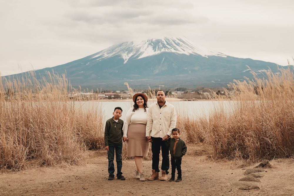A group stands together in front of Mount Fuji on a serene winter day with dried grass swaying in the foreground.