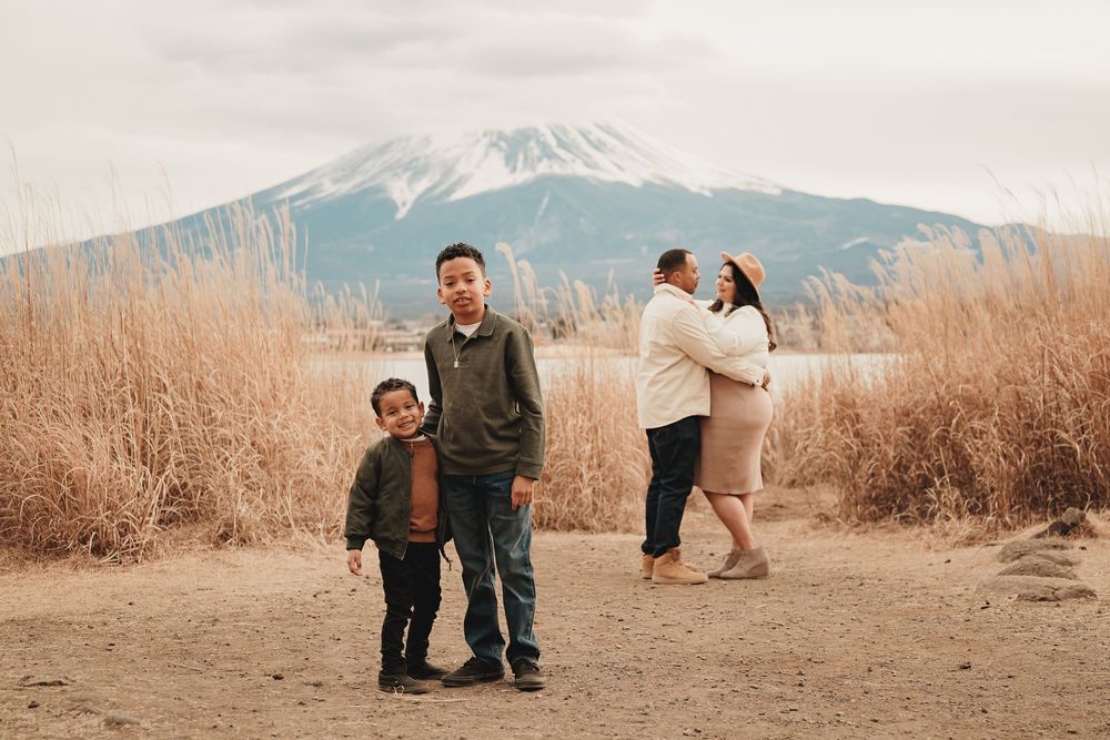Family enjoying a winter day with Mount Fuji in background, surrounded by tall brown grass.