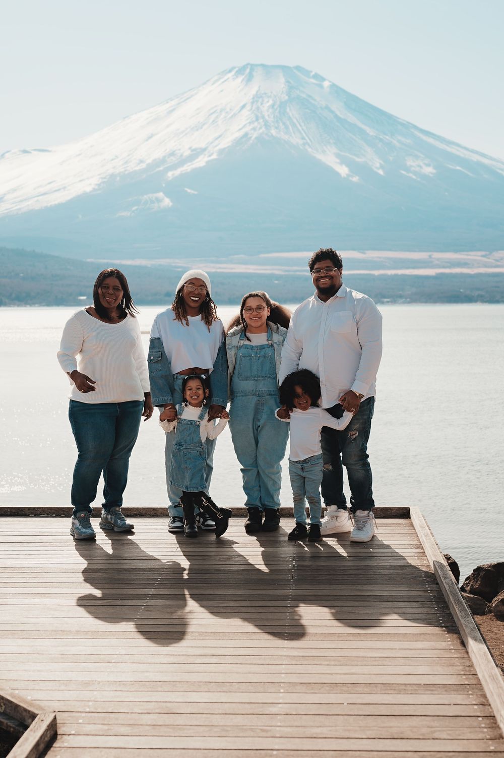 A family sits together on a wooden dock overlooking a snowy mountain and lake on a peaceful winter day.