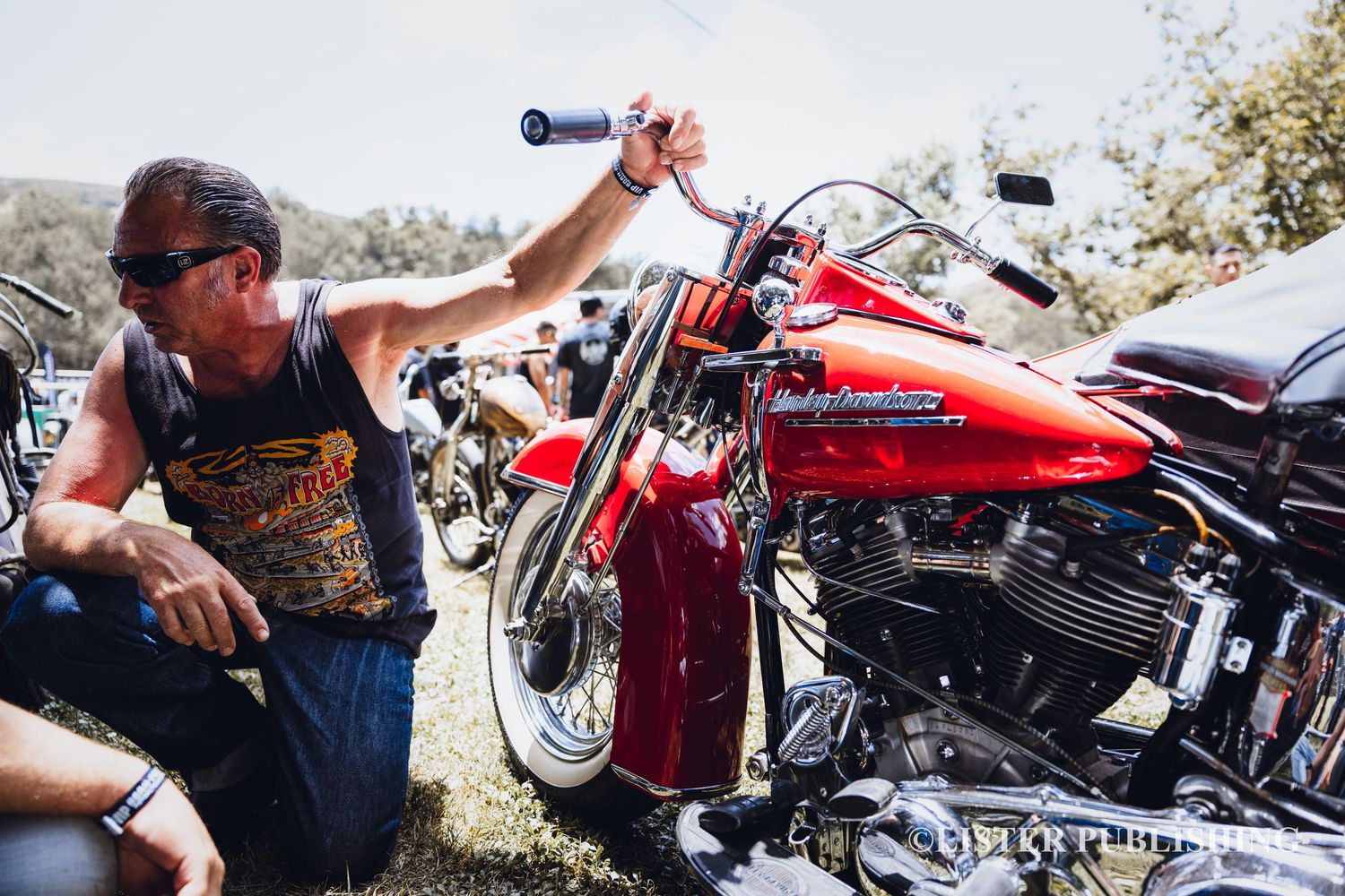Person working on customizing red Harley Davidson motorcycle at outdoor event.