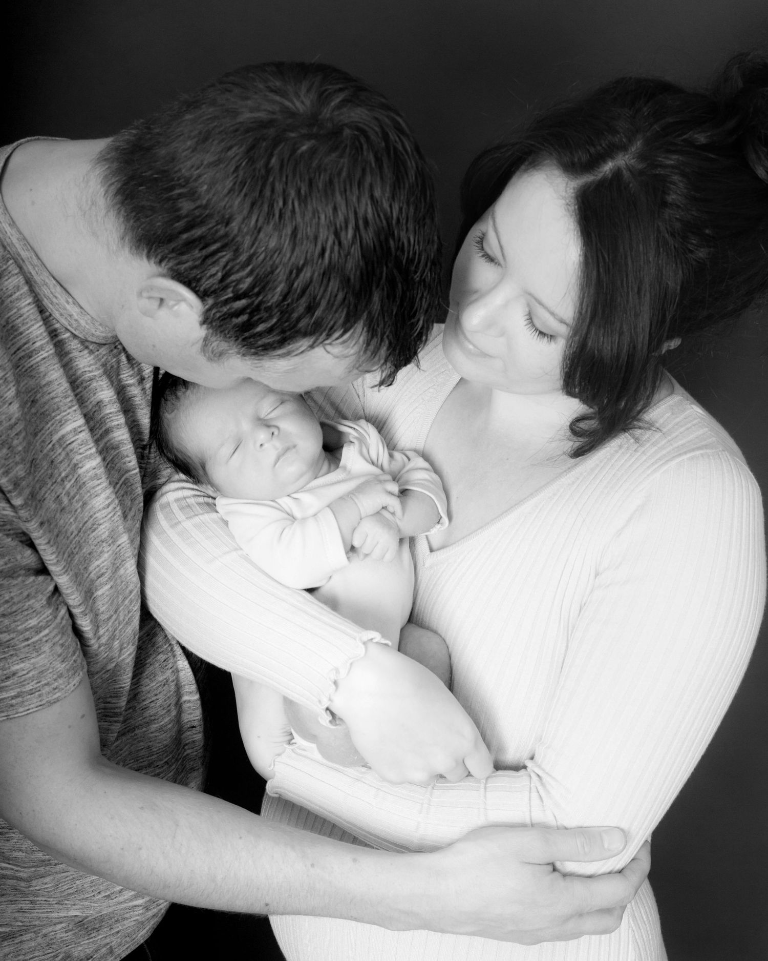 A couple lovingly cradles their newborn in a black and white image, taken by Abigail's Studio in Buckinghamshire.