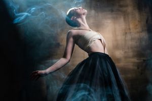 Emotive photograph of a woman wearing bandages and dramatic black skirt with smoke effects.