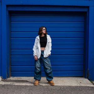 Editorial fashion portrait of a woman in front of a blue urban backdrop.