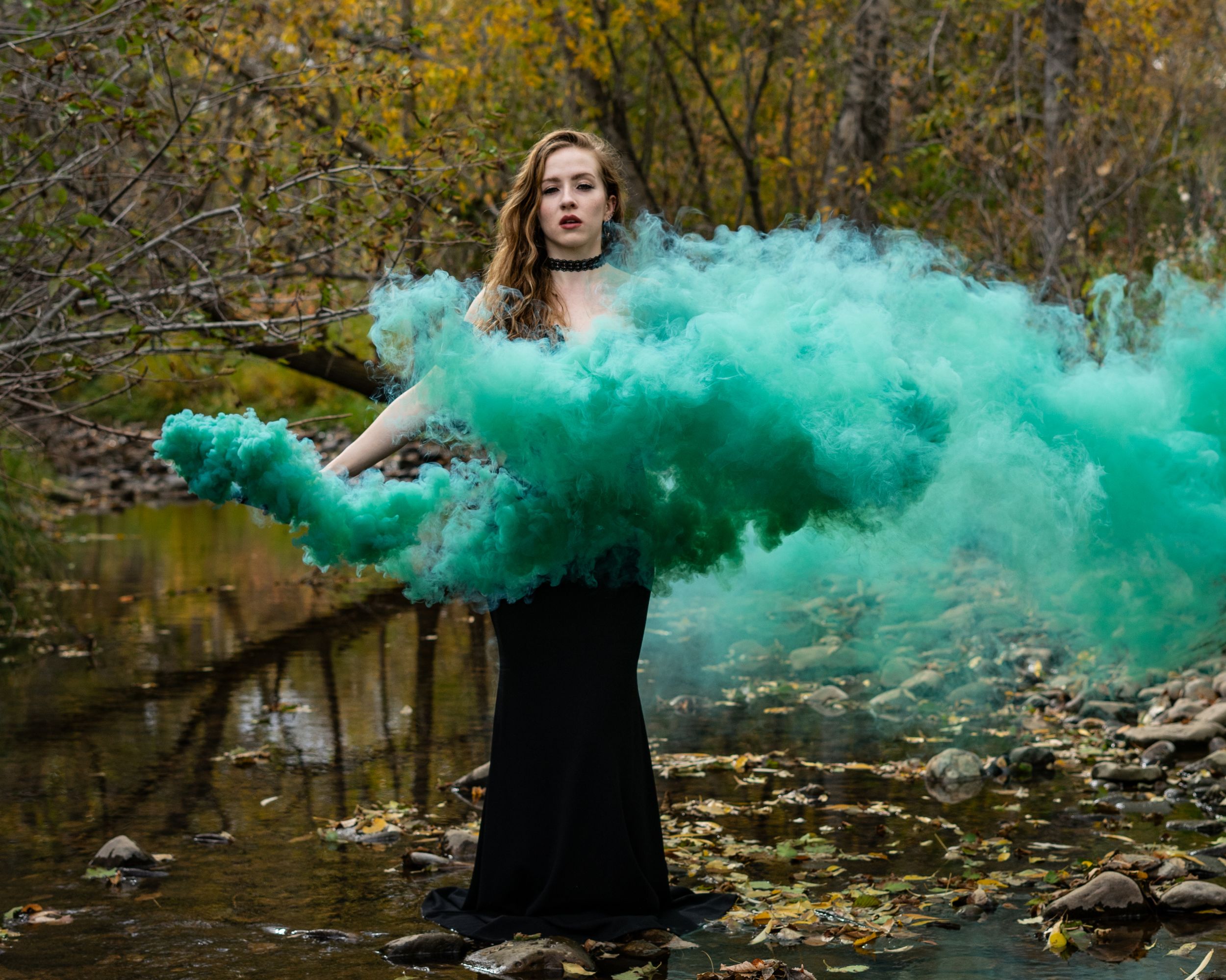 Green smoke bomb portrait of a woman in an elegant black dress with autumn tree background.
