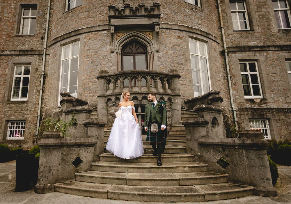 Wide stone staircase leads to ornate Gothic castle entrance with figures on steps and decorative architecture details.