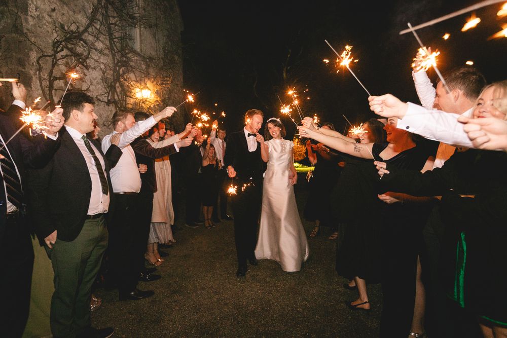 Wedding guests create a sparkler tunnel as the bride and groom exit their celebration at night.