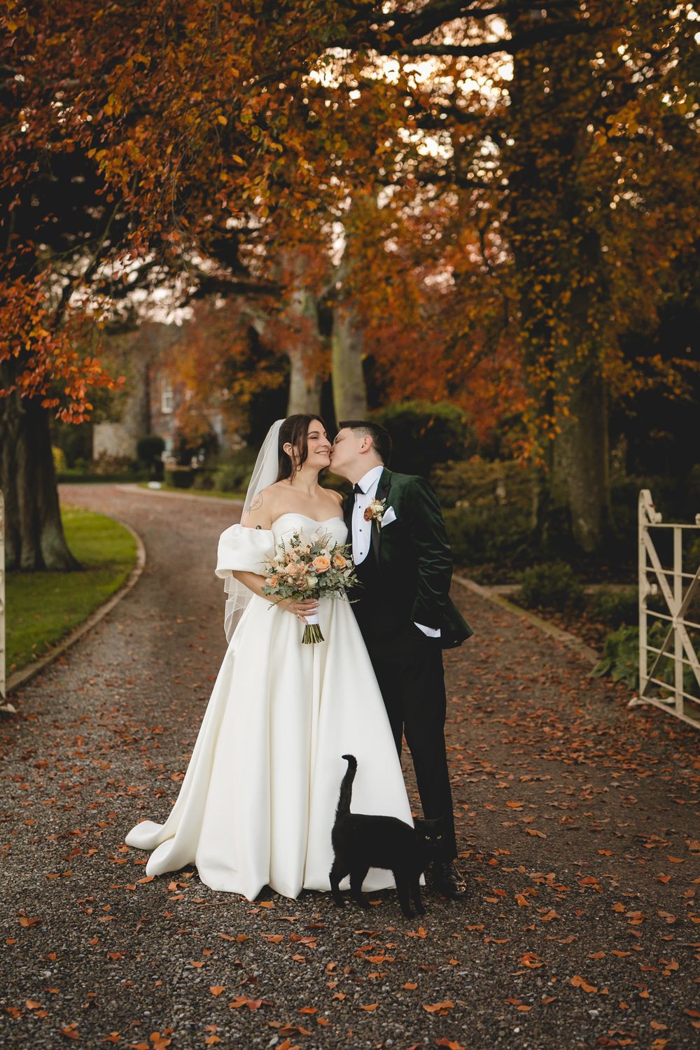 A romantic autumn wedding scene with fallen leaves on a tree-lined path during golden hour.