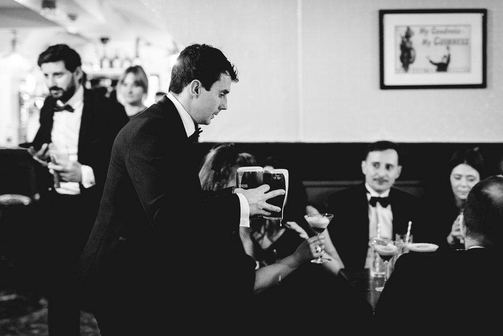 Black and white photograph of people socializing while seated and standing at tables in a formal restaurant setting.