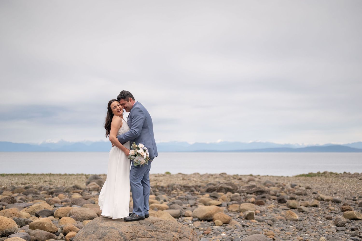 A bride and group embrace on a rocky beach