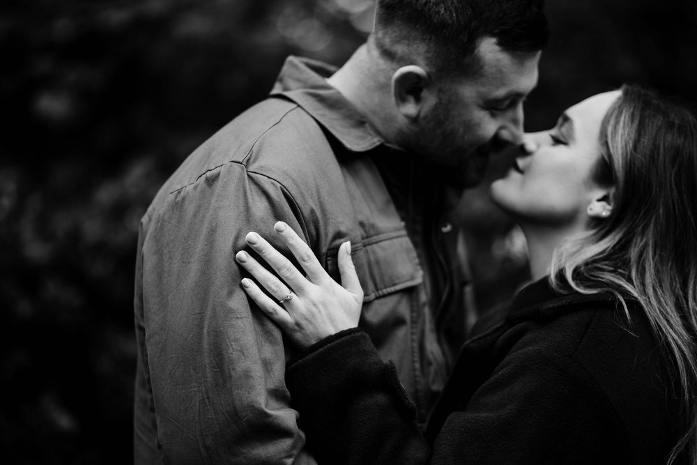 Black and white photo of a romantic couple sharing a tender kiss outdoors, woman wearing an engagement ring - Lynette Matthews Photography