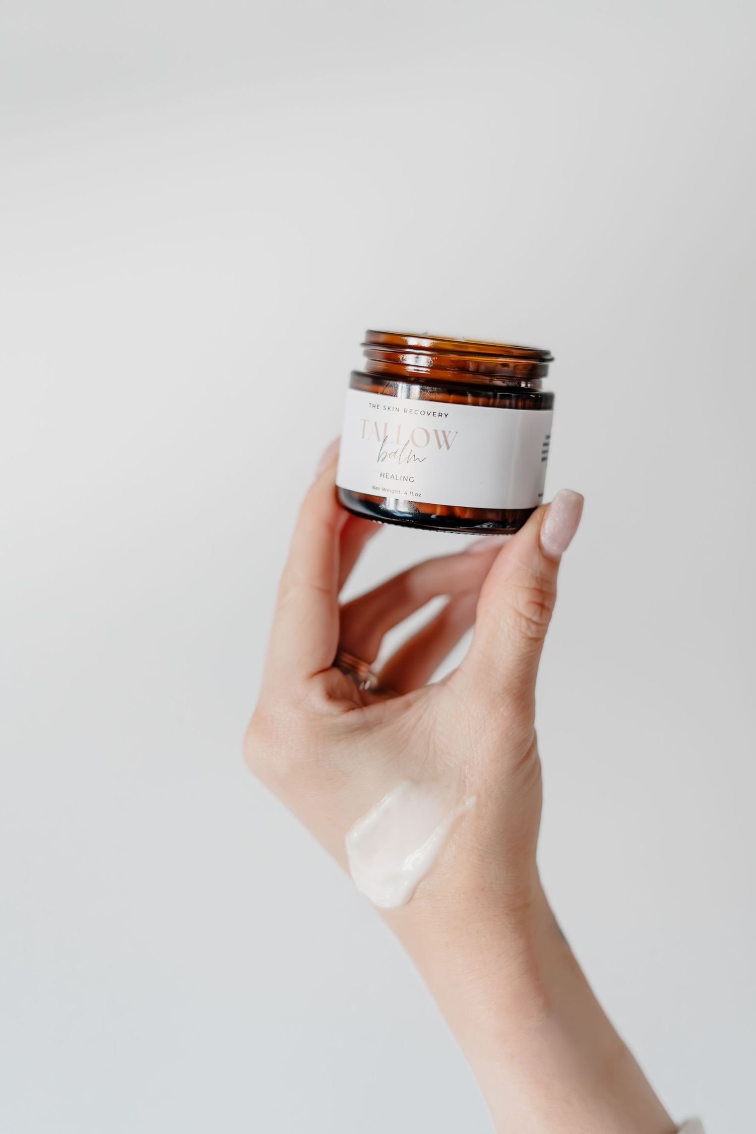 Hand holding small amber glass jar against white background.