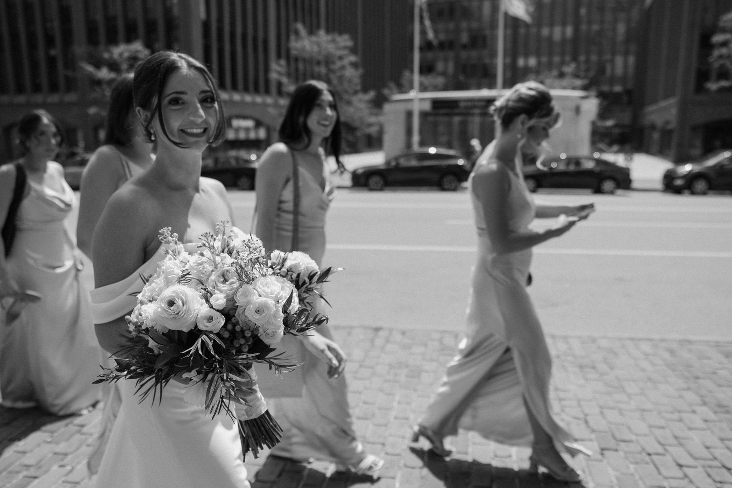 Wedding party walks along cobblestone street outside historic building.