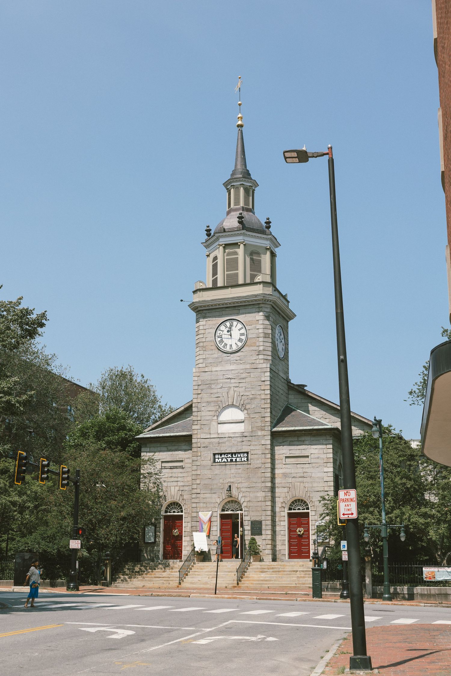 Historic stone church with clock tower and red doors under bright blue sky.