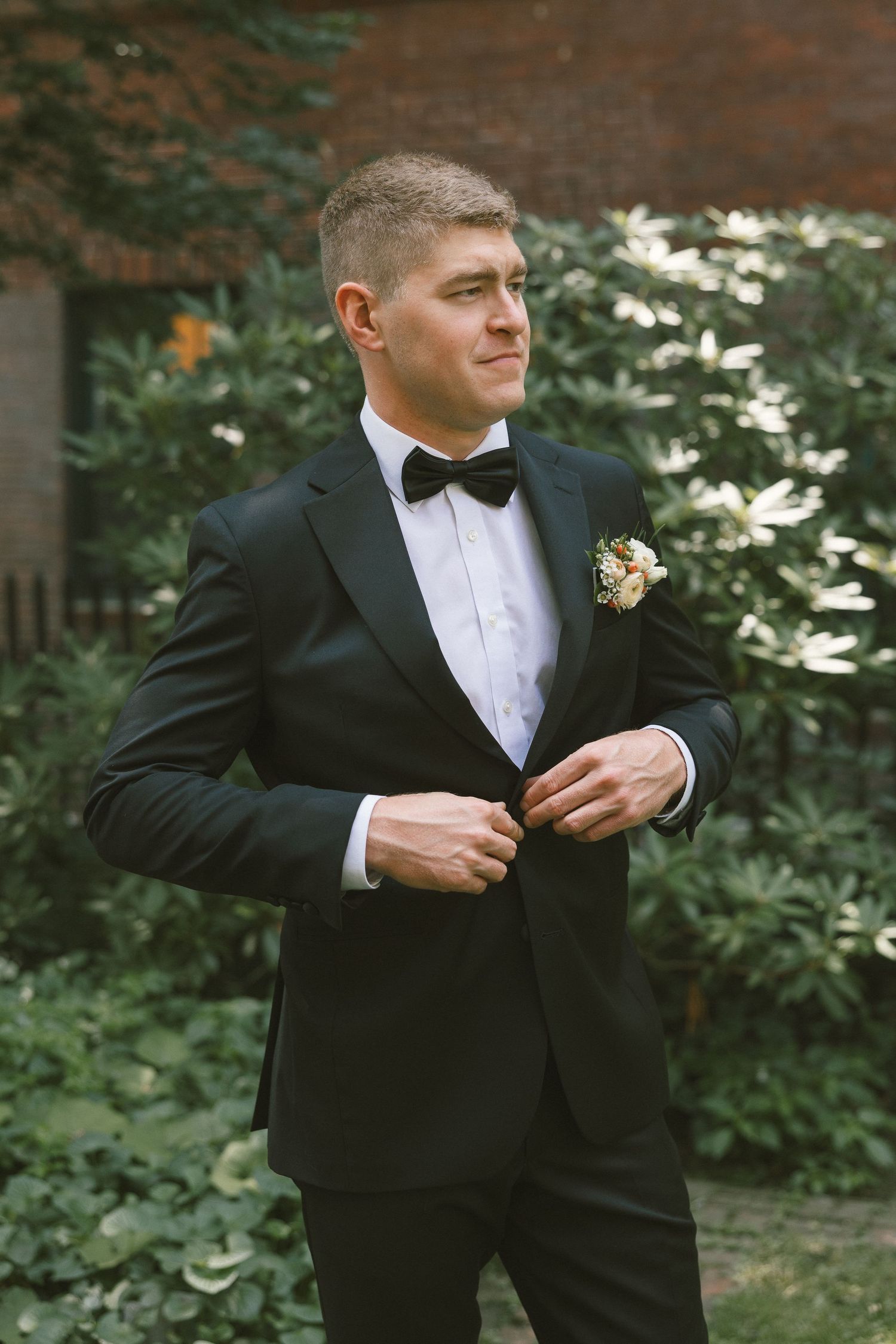 Person adjusts formal black tuxedo and bowtie while getting ready.