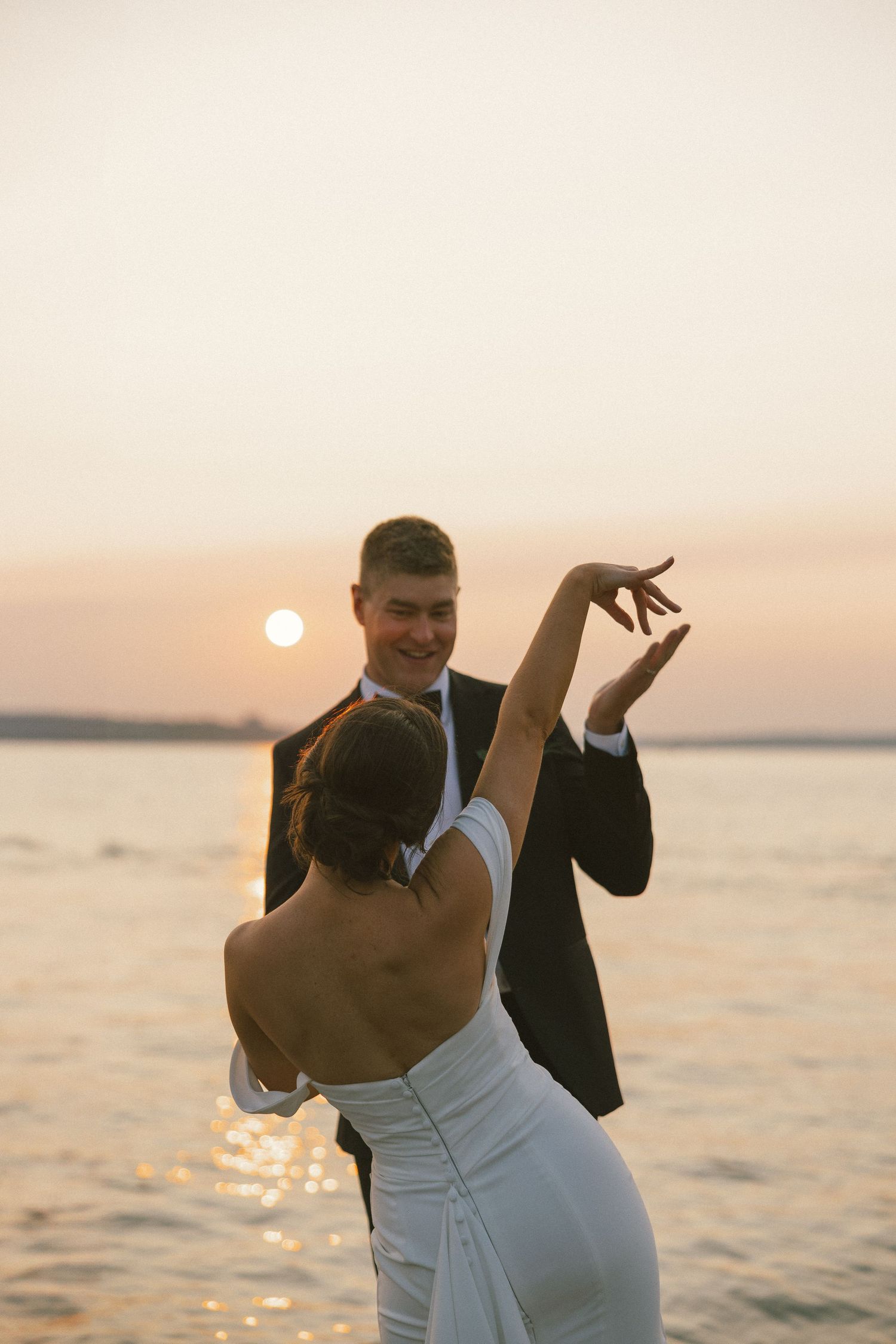 Couple dancing together at sunset with golden light reflecting off the water behind them.