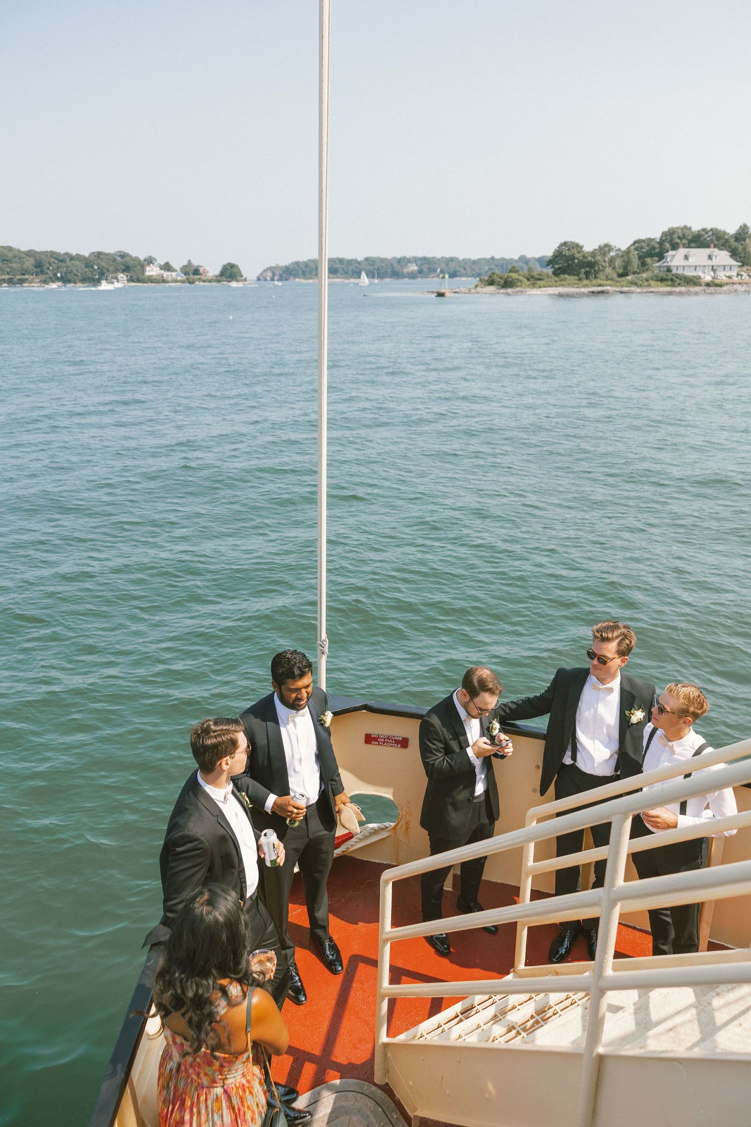 Wedding party members in formal attire gathered on boat deck overlooking water.