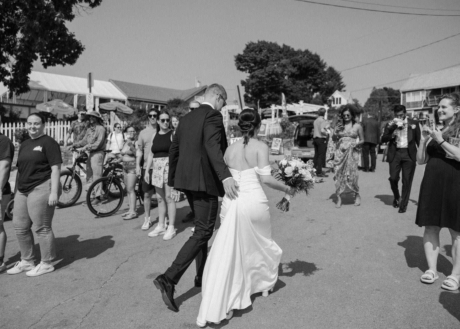 Black and white photo of wedding party walking along crowded street.