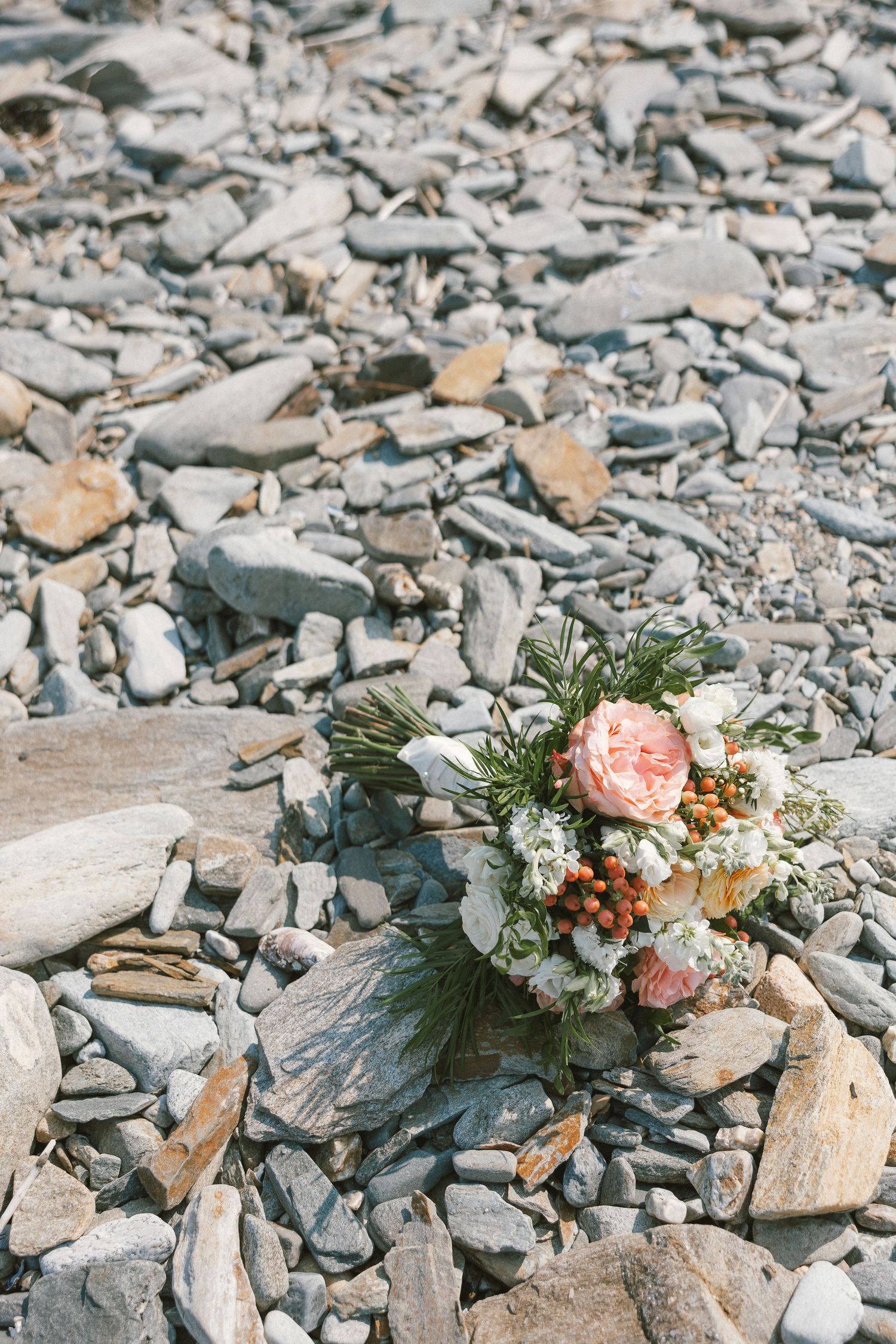 Delicate floral bouquet with pink roses and white flowers resting on rocky coastal terrain.