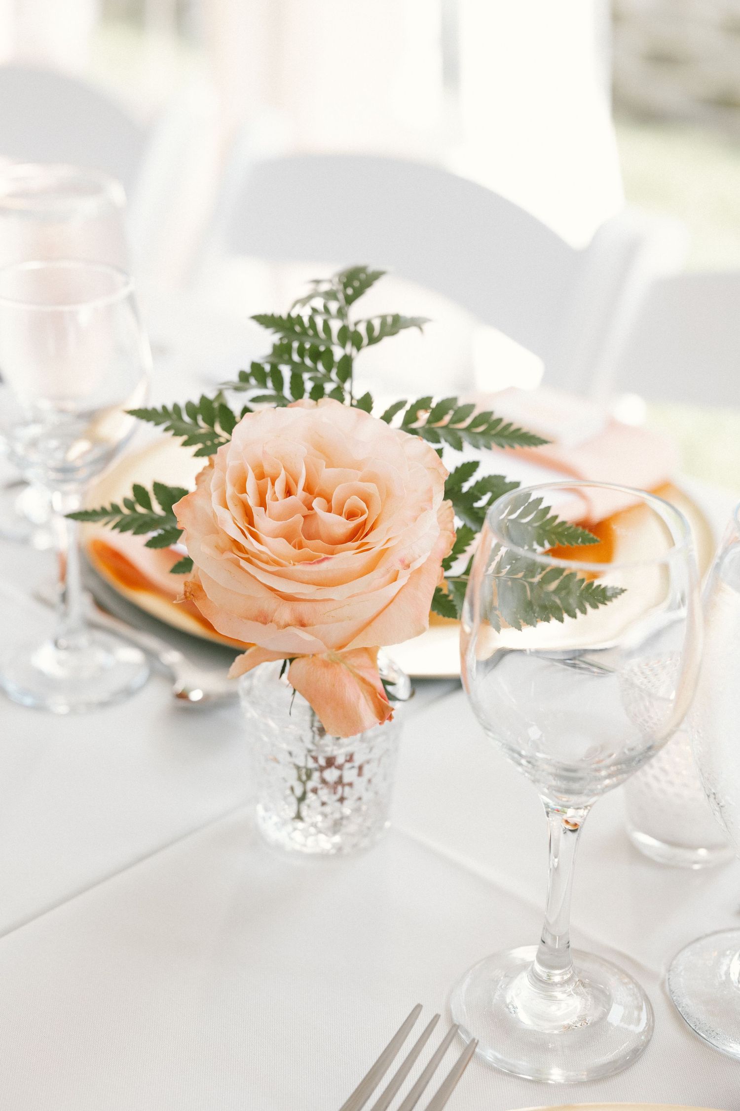 Elegant table setting with peach roses and crystal glassware on white tablecloth.