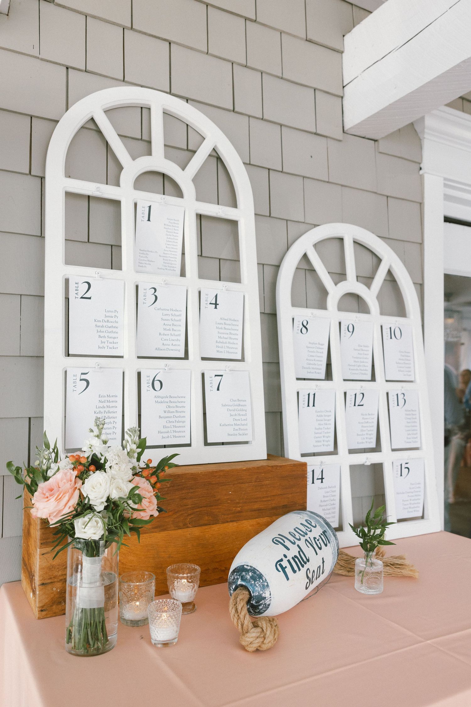 Wedding seating chart display with white arched frames and floral decorations.