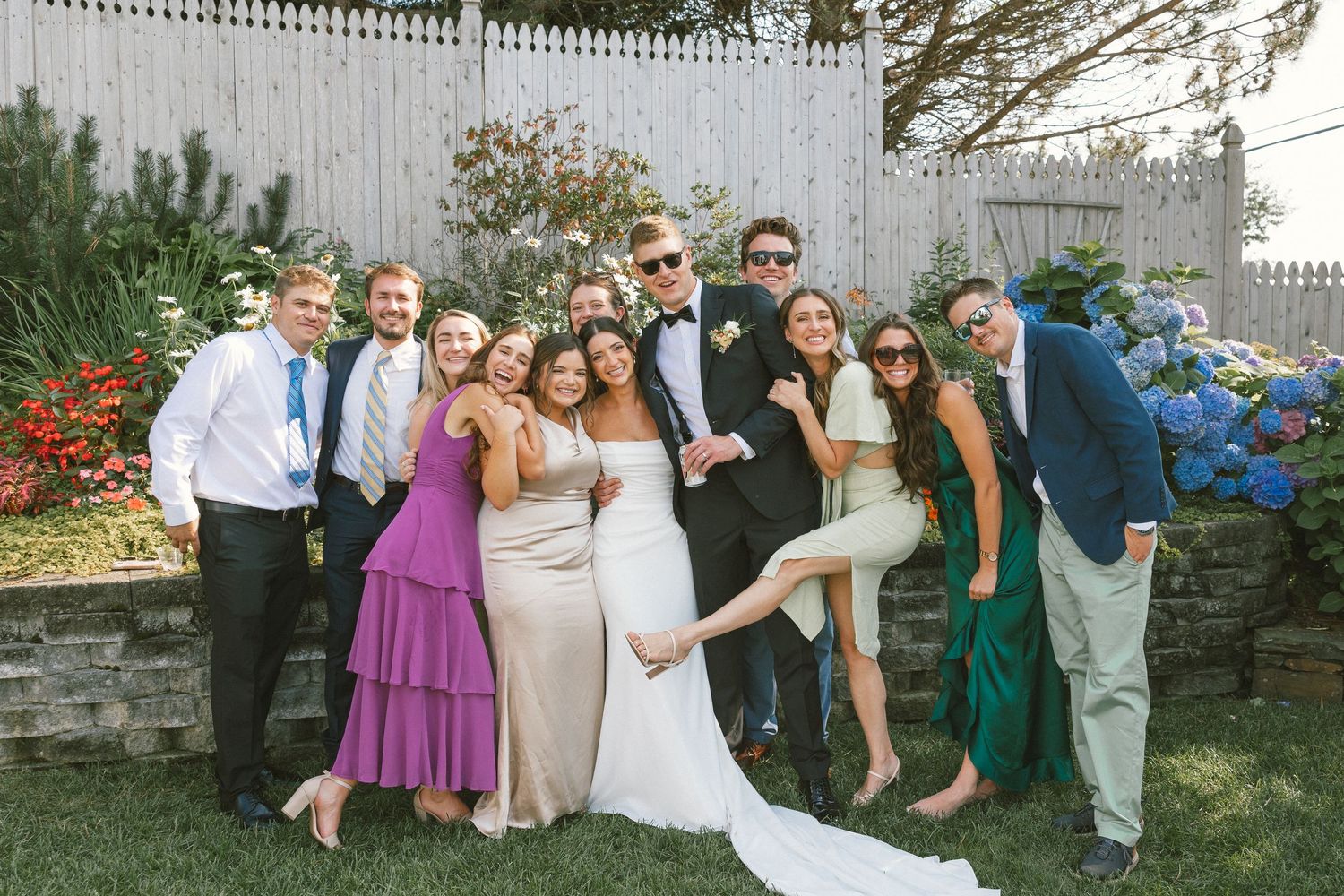 Wedding party group photo with colorful attire in an outdoor garden setting.