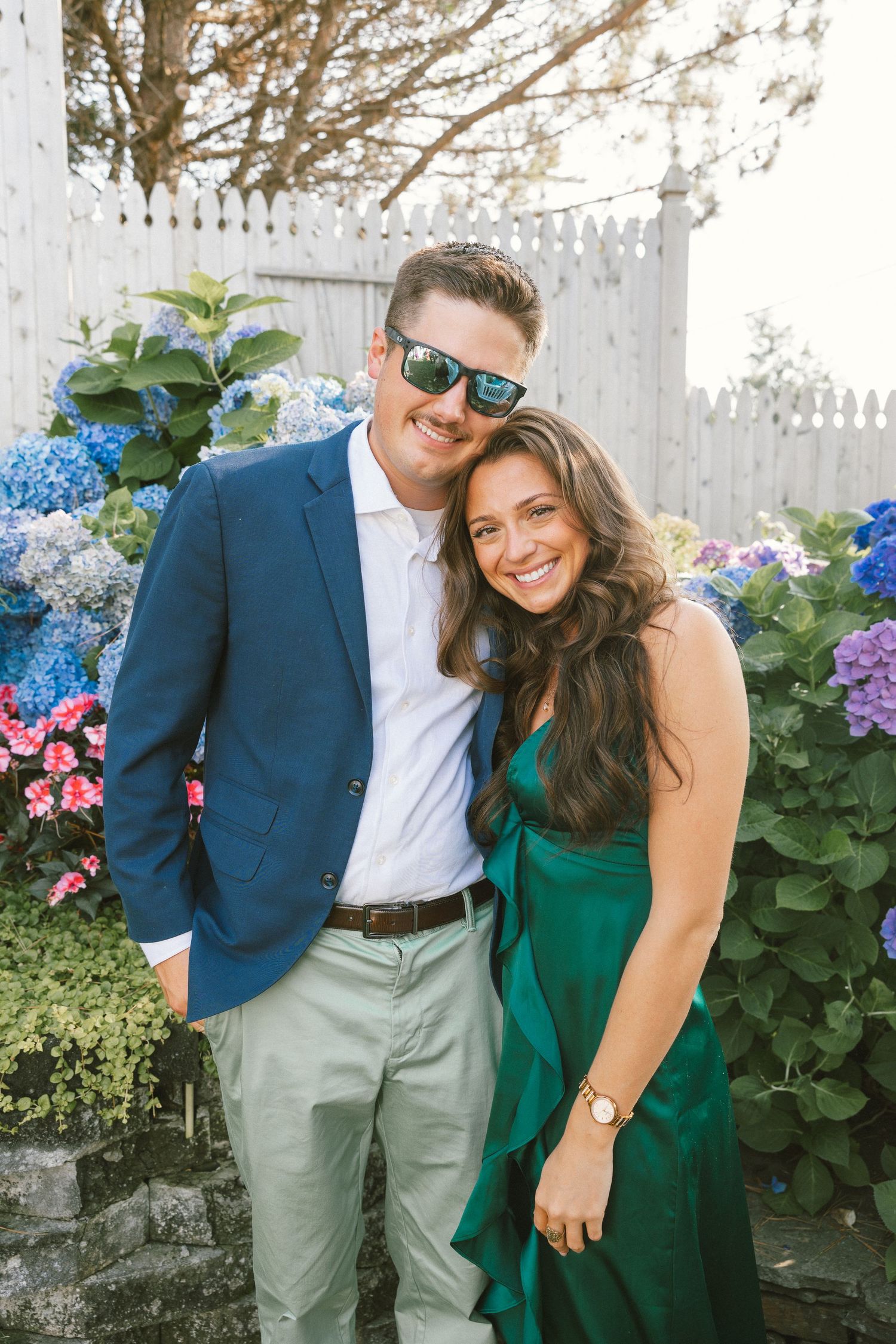 Couple in blue suit and green dress posing by flowering hydrangea bushes.