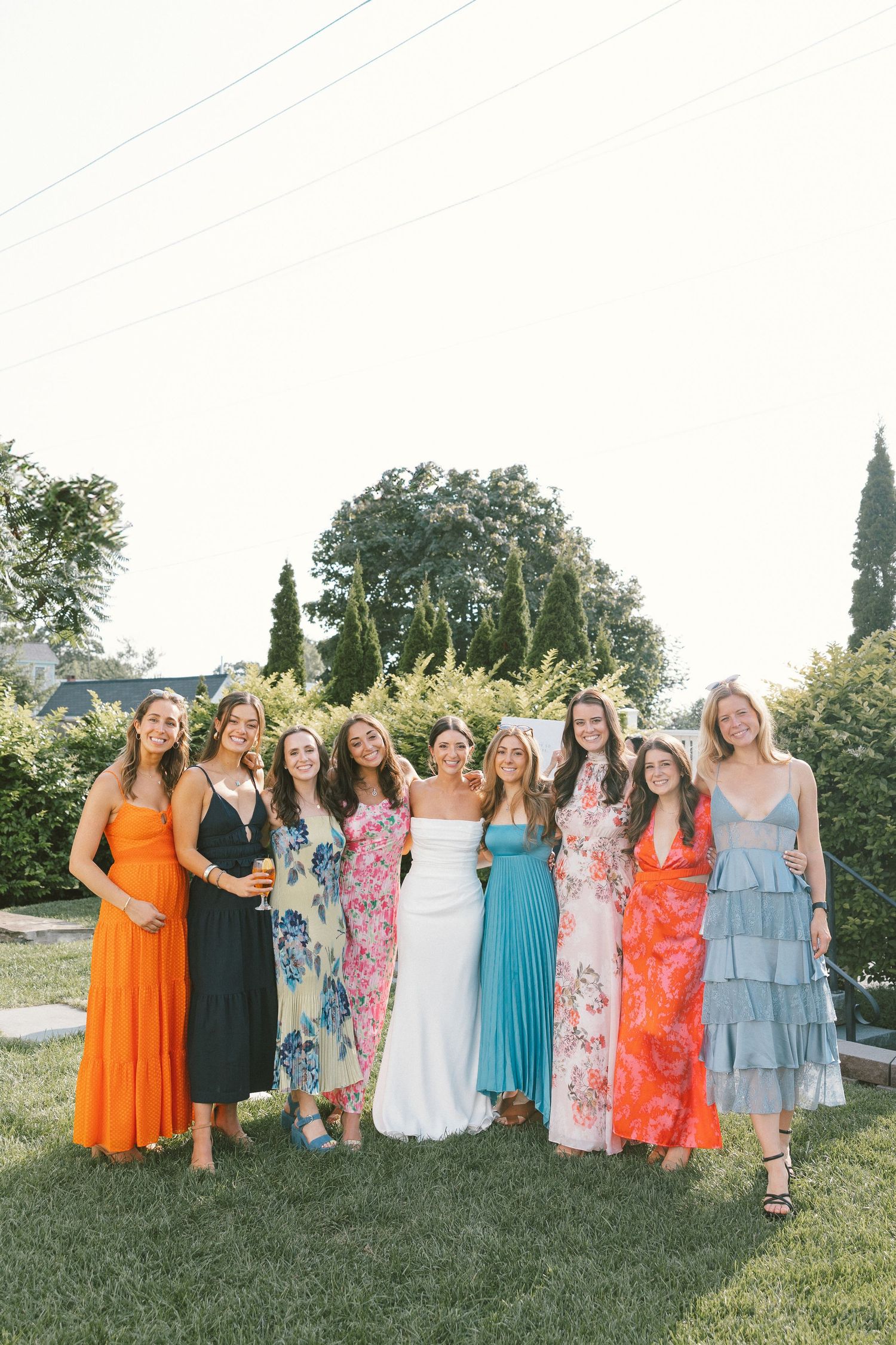 Bridal party in colorful summer dresses posing together on grassy lawn.