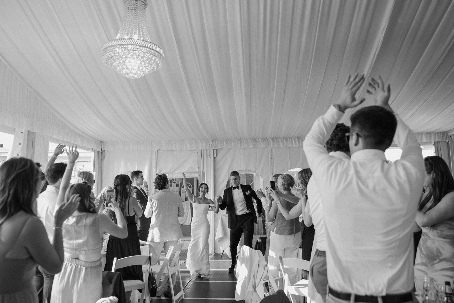 Wedding reception celebration under white draped tent with crystal chandelier.