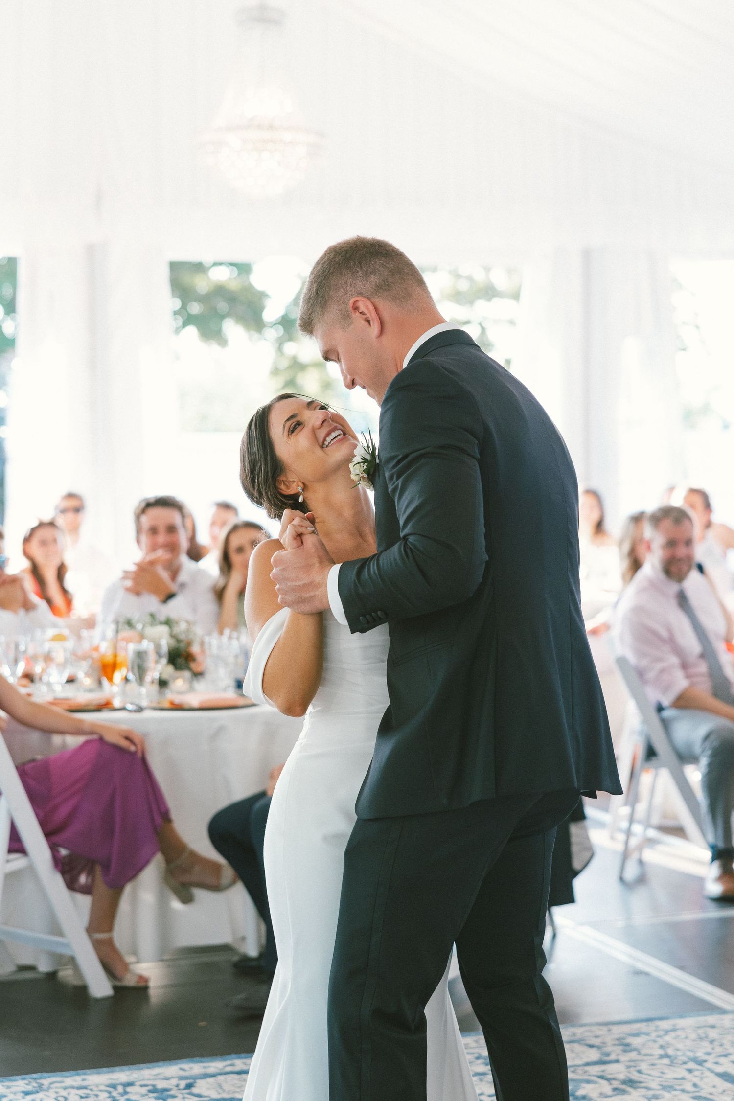 Couple sharing a romantic first dance at their wedding reception while guests look on from tables in the background.