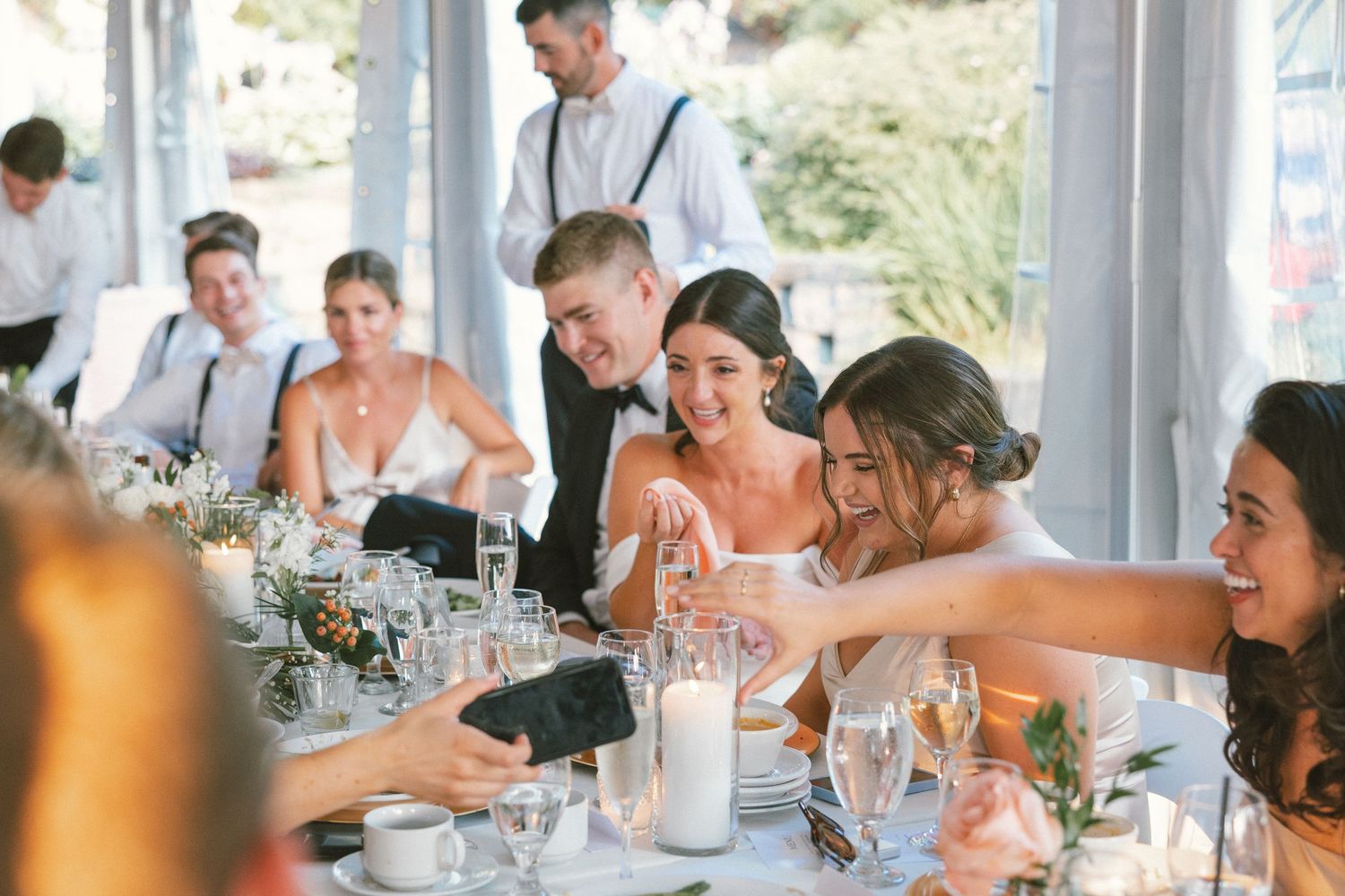 Wedding guests laughing and raising glasses during a reception celebration.