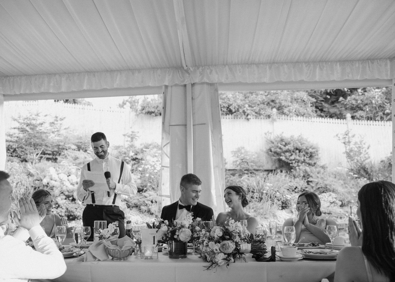 Wedding guests enjoying dinner and conversation at a reception under a white tent.