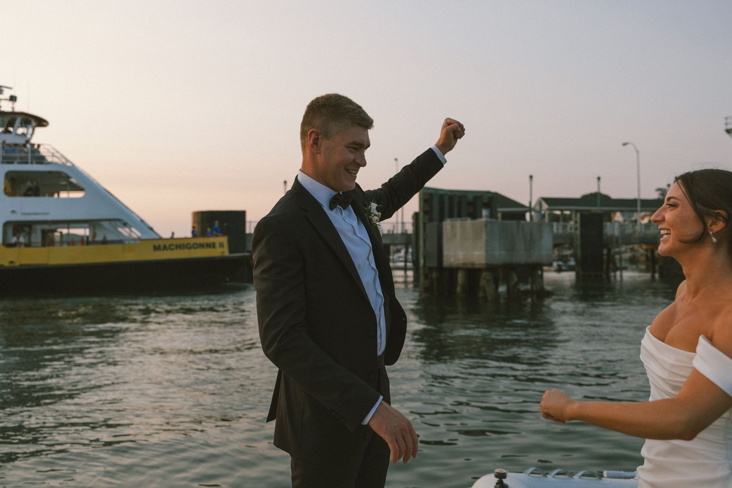 Couple dancing together on a dock at sunset with water and boats in the background.