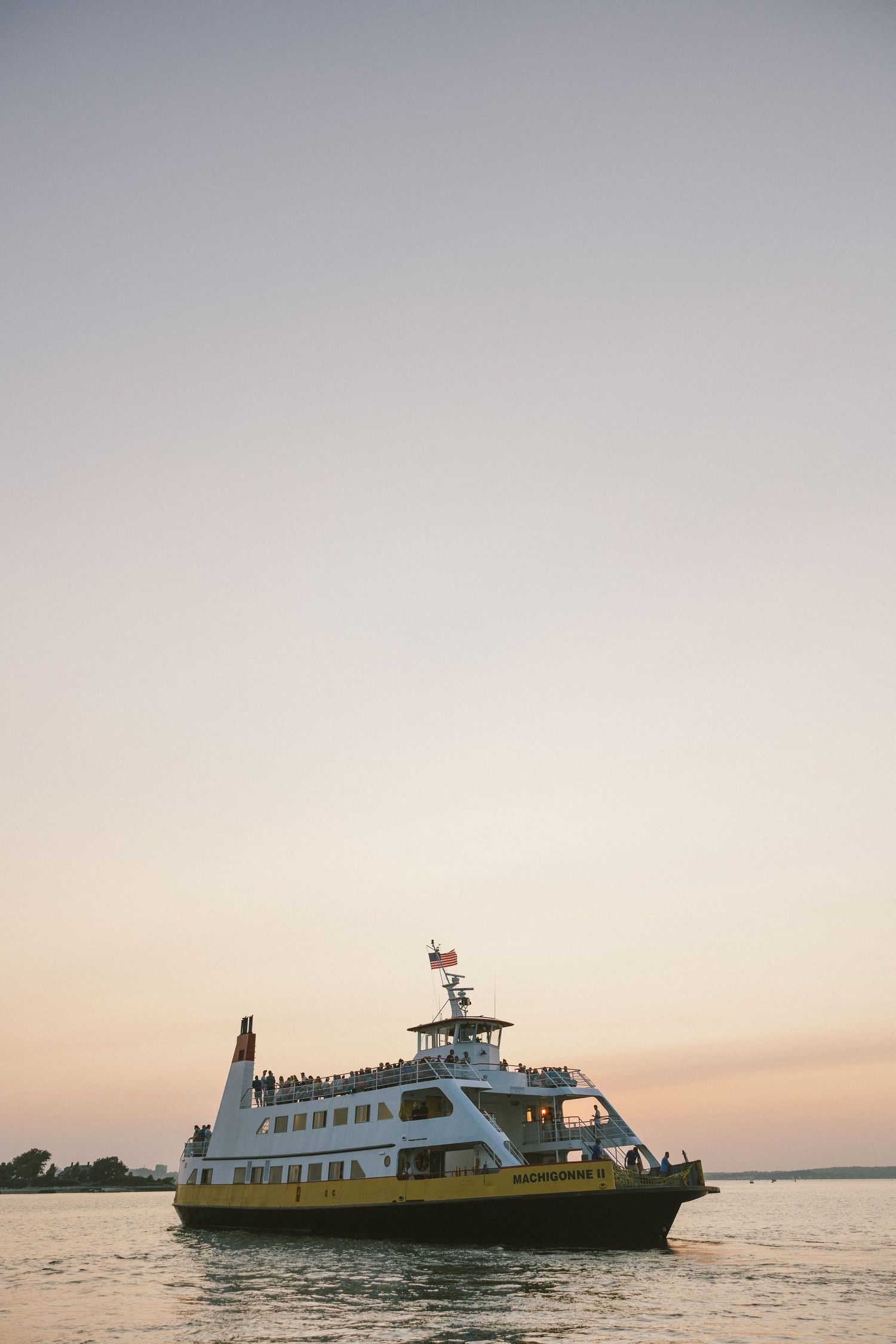 Yellow and white ferry boat sailing across calm waters during sunset.