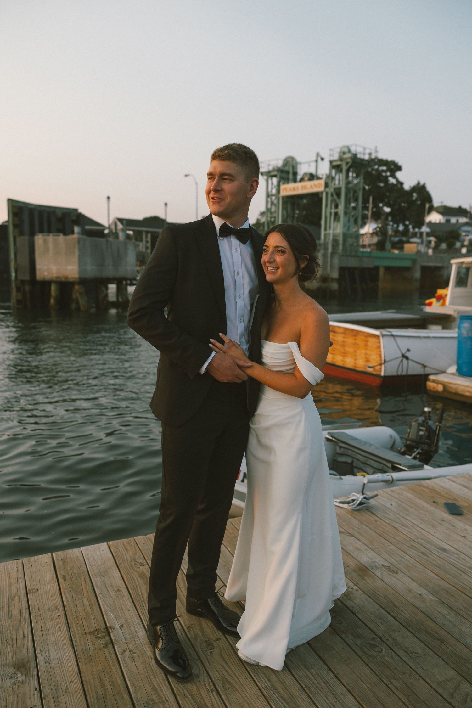 Wedding couple posing for photos on a wooden dock with boats and water in the background.