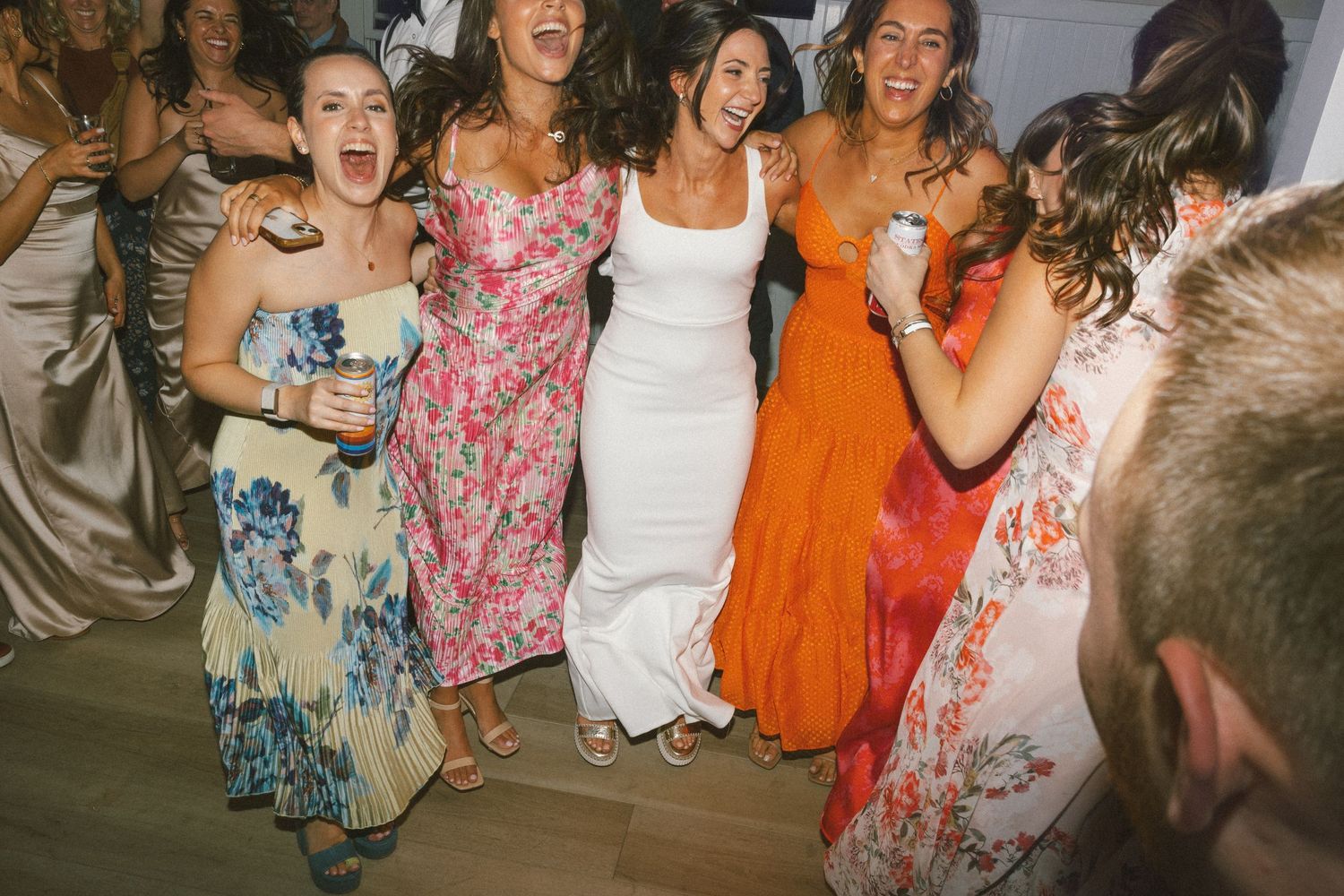 Wedding guests dancing and celebrating joyfully in colorful dresses at reception.