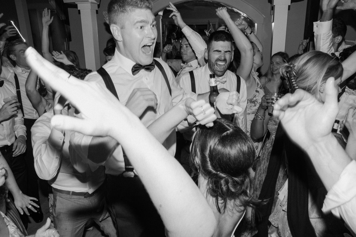 Wedding guests dancing energetically in black and white at reception party.